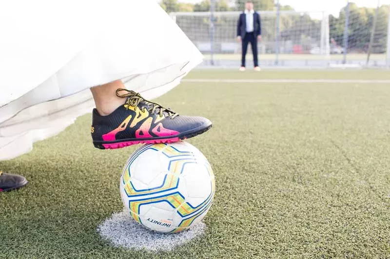 Braut mit Fußballschuhen und Ball bei Hochzeitsfotos im Fußballstadion