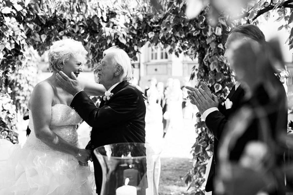 Emotionale Hochzeit im Schlosshotel Grunewald, die einen rührenden Moment zwischen Braut und Bräutigam unter einem Laubbogen zeigen.