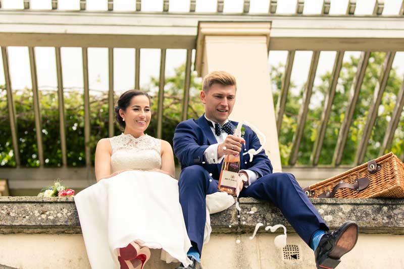 Das Brautpaar sitzt auf den Stufen von Schloss Glienicke und genießt Champagner, während sie für das Fotoshooting posieren.