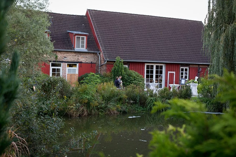 Idyllische Außenansicht des Landhauses Alte Schmiede mit einem Teich im Vordergrund.