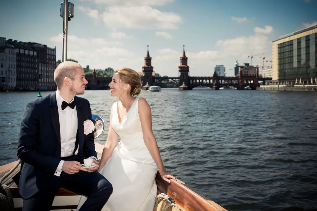 Brautpaar während der Bootsfahrt bei der Hochzeit am Schloss Friedrichsfelde mit Blick auf die Oberbaumbrücke.