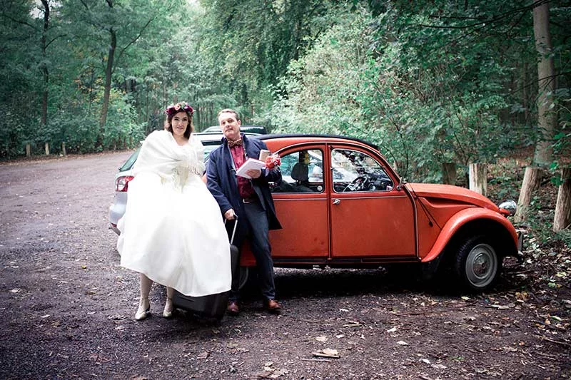 Braut und Bräutigam neben einem roten Vintage-Auto auf einem Waldparkplatz, Ankunft zur Hochzeit in der Villa Blumenfisch.