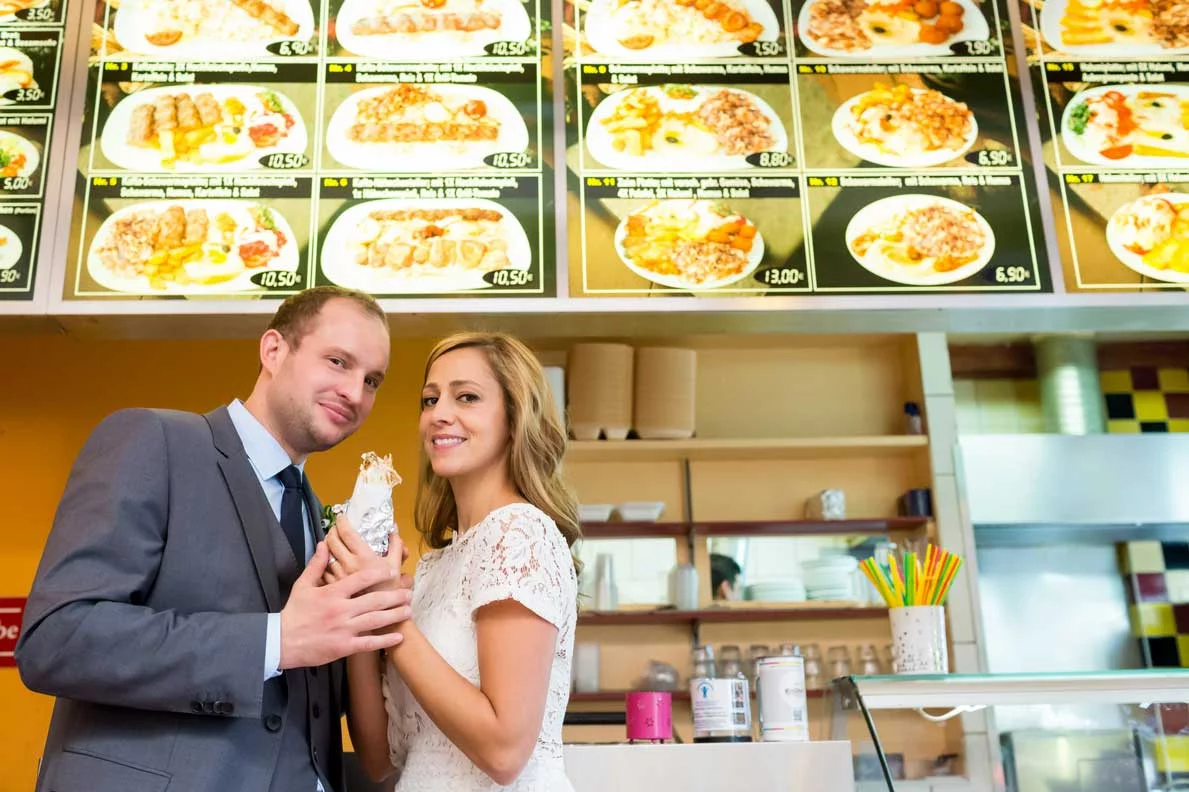 Das Brautpaar gönnt sich nach der standesamtlichen Trauung einen Döner in einem Berliner Imbiss, humorvolle Hochzeitsfotos in Schöneberg.
