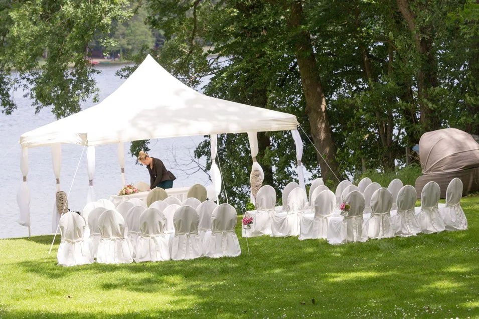 Eine Hochzeit im Garten des Landhauses Himmelpfort, mit einem weißen Zelt und Stühlen, umgeben von Bäumen und mit Blick auf den See.