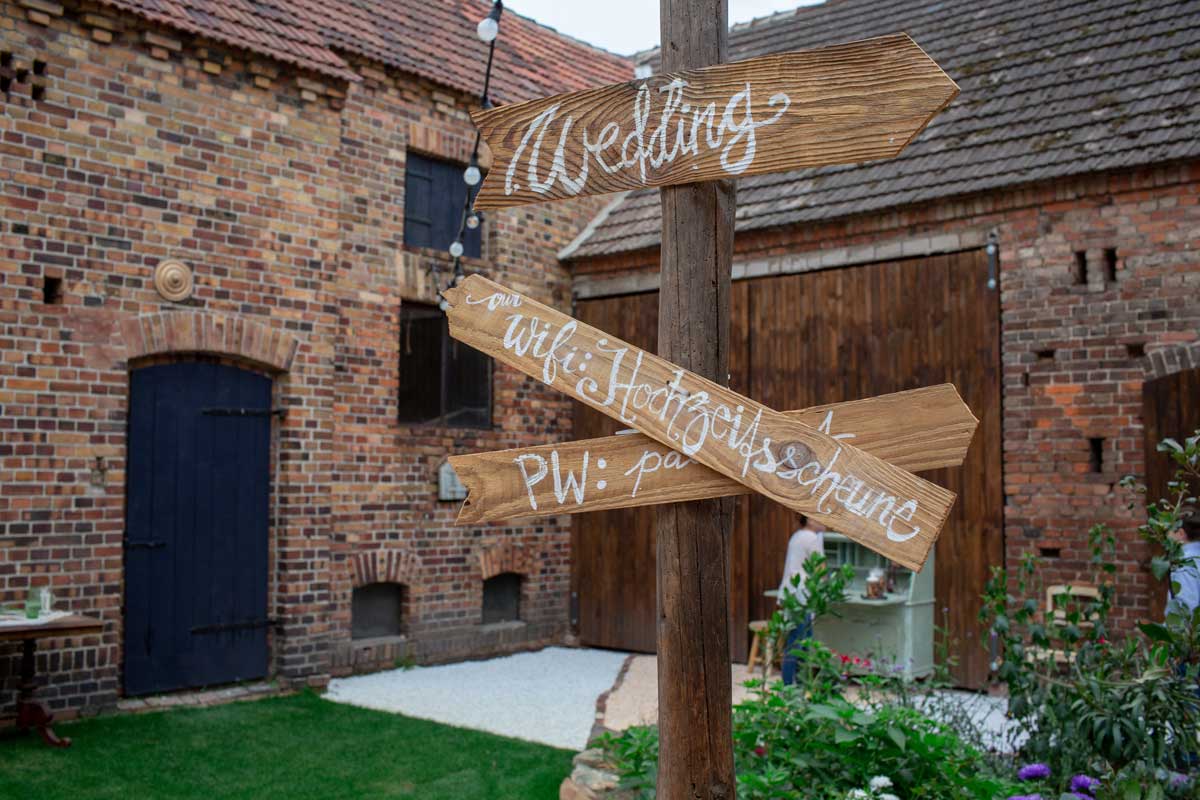 Hochzeitsschild aus Holz in der Hochzeitsscheune Glücksburg mit handgeschriebenen Beschriftungen und rustikaler Backsteinkulisse.
