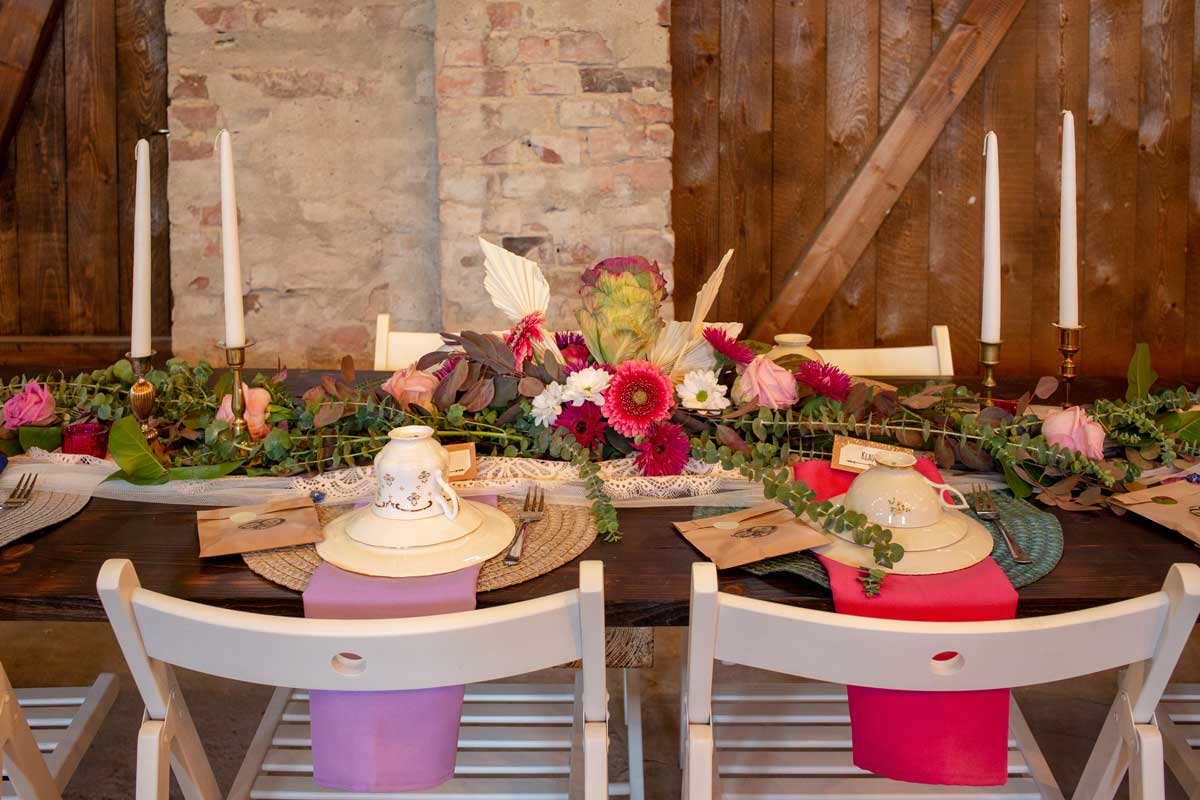 Festlich gedeckter Tisch in der Hochzeitsscheune Glücksburg, geschmückt mit Blumen, Kerzen und stilvollem Geschirr vor rustikaler Backsteinkulisse.