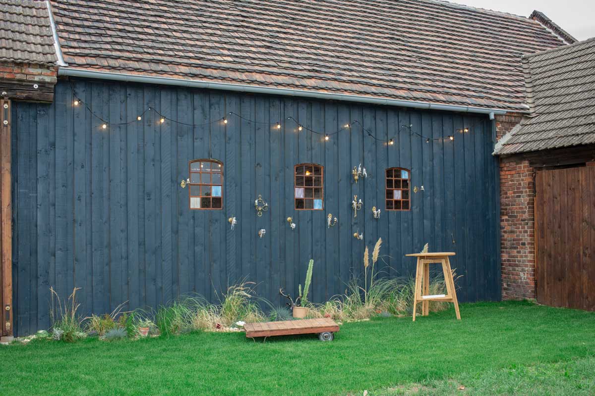 laue Holzwand in der Hochzeitsscheune Glücksburg, dekoriert mit Wandkerzenhaltern und Lichterketten, idealer Hintergrund für eine Fotobox.

