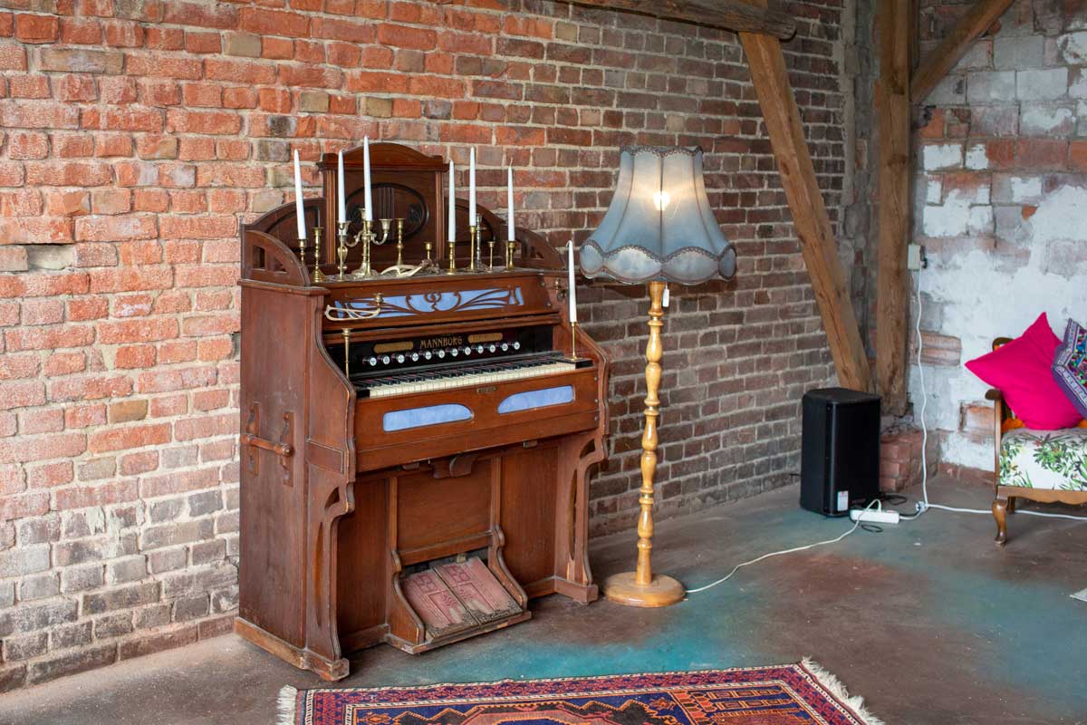 Altes Harmonium und nostalgische Stehlampe in der Hochzeitsscheune Glücksburg vor rustikaler Backsteinkulisse.