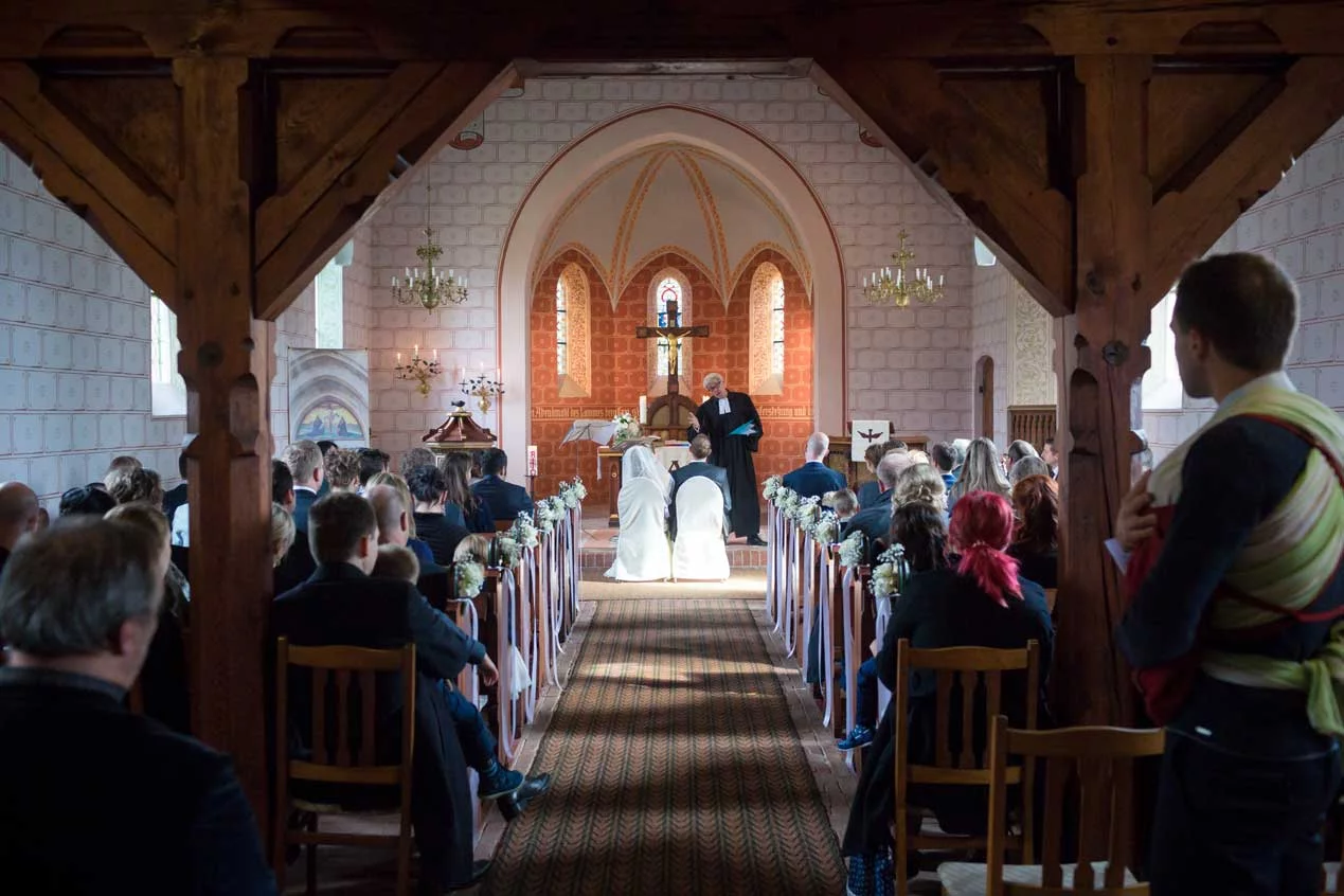 Das Brautpaar kniet vor dem Altar während der Hochzeitszeremonie in einer festlich dekorierten Kirche, Hochzeitsfotos Schloss Kartzow.