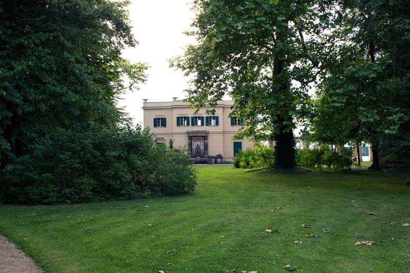 Gesamtansicht des Schlosses Glienicke, umgeben von üppigem Grün und gepflegten Rasenflächen.