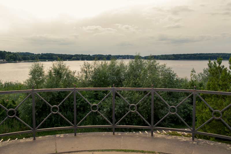 Aussicht vom Schloss Glienicke auf den Wannsee, mit einem schmiedeeisernen Geländer im Vordergrund und üppiger Vegetation.