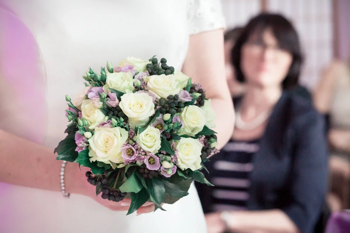 Hochzeit SeePavillon am Tegeler See – Detailaufnahme des Brautstraußes mit cremeweißen Rosen und lila Blüten, gehalten von der Braut.